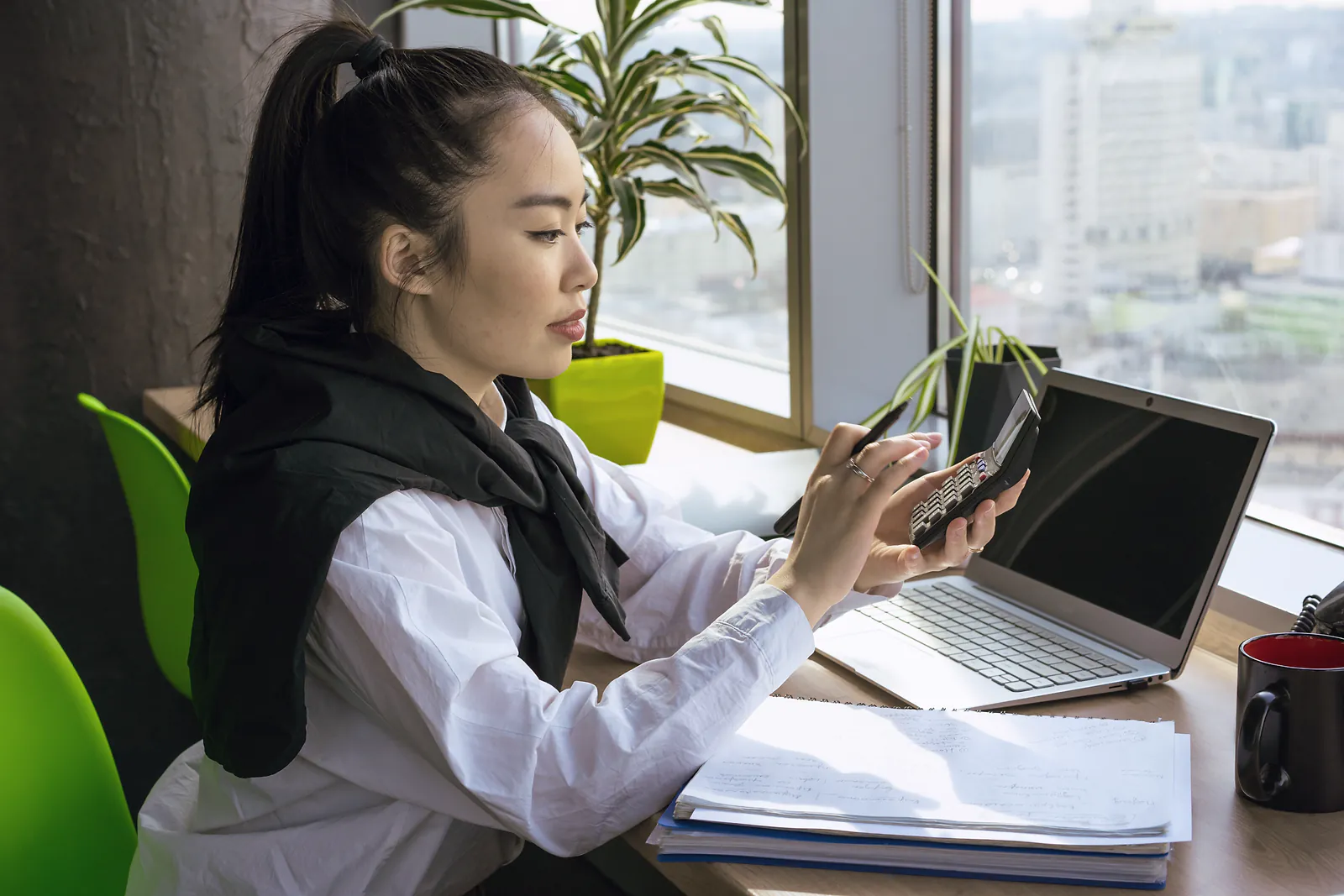 An accountant checks figures on a calculator beside her laptop and working papers
