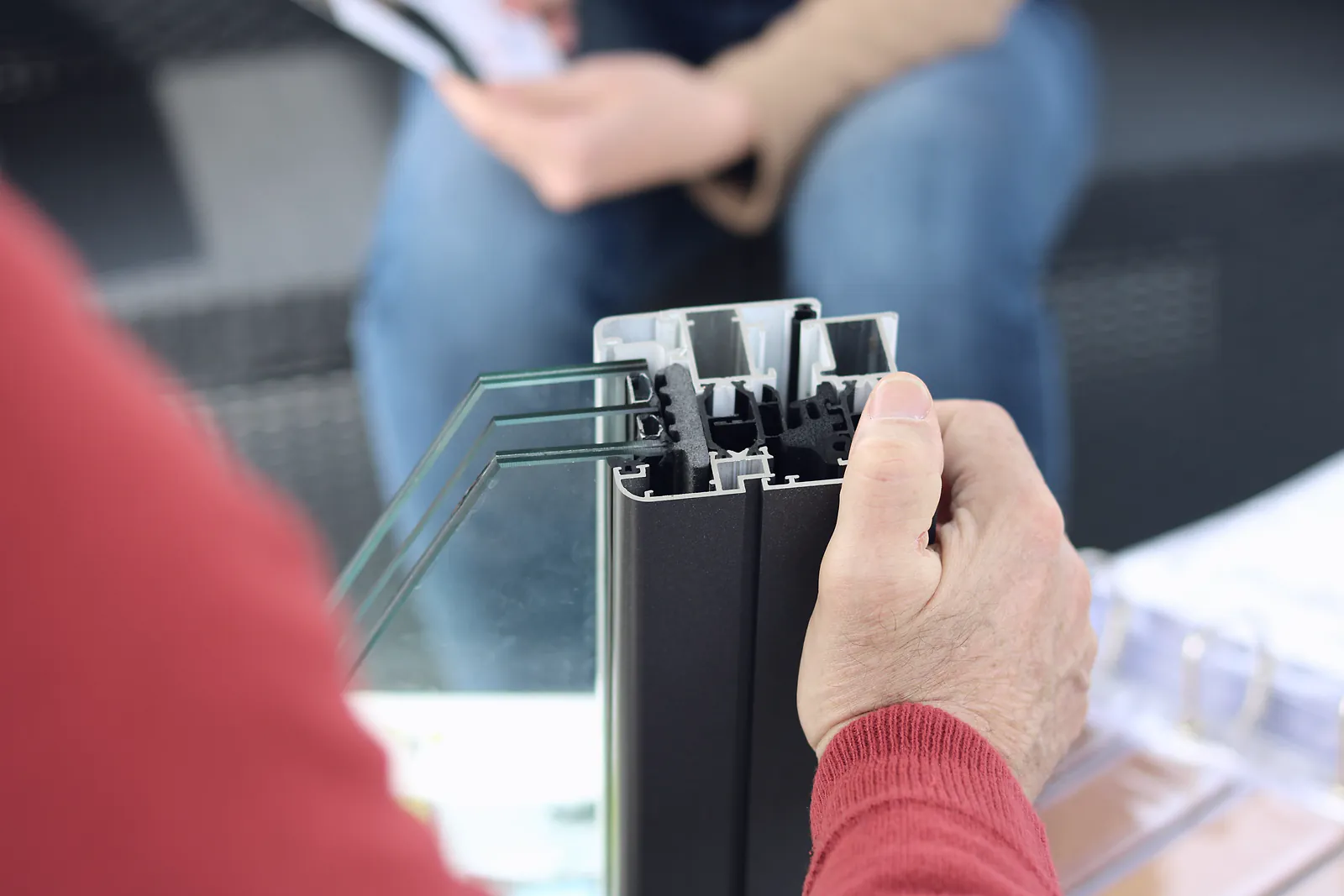 A hand holds a cut section of a double-glazed aluminium window frame