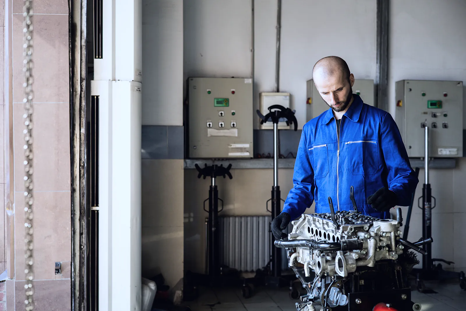 A mechanic in blue overalls works on a stripped engine block in a workshop