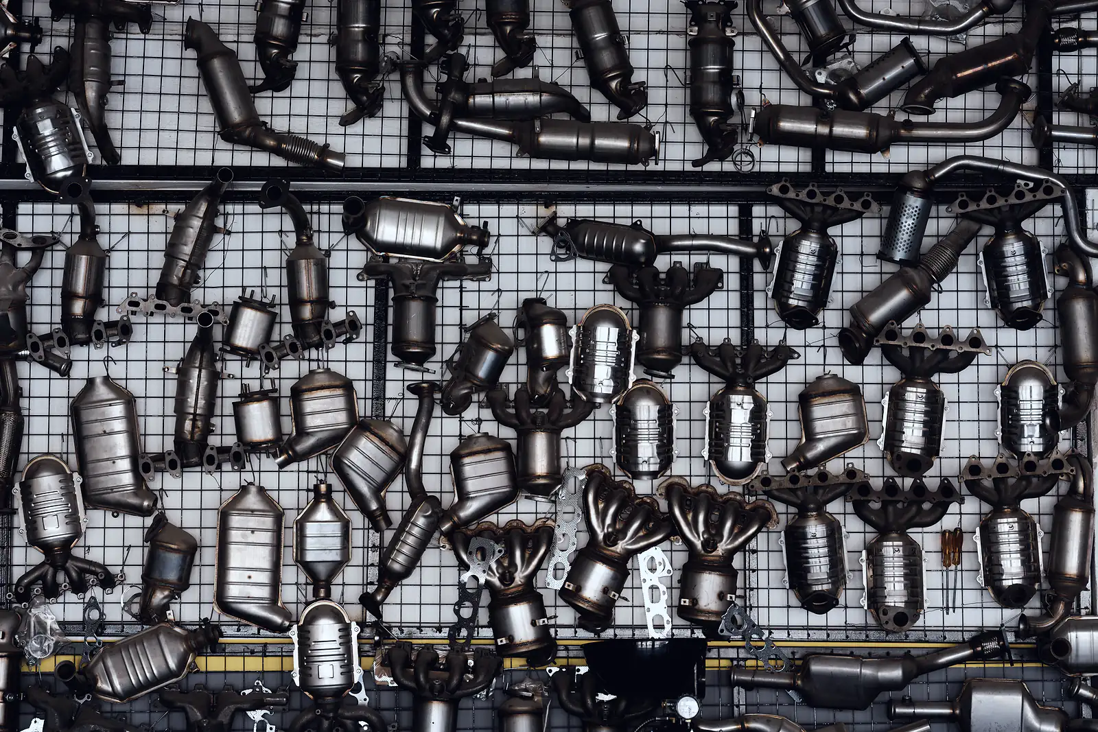 Exhaust manifolds and catalytic converters hang in rows on a parts trader's mesh wall