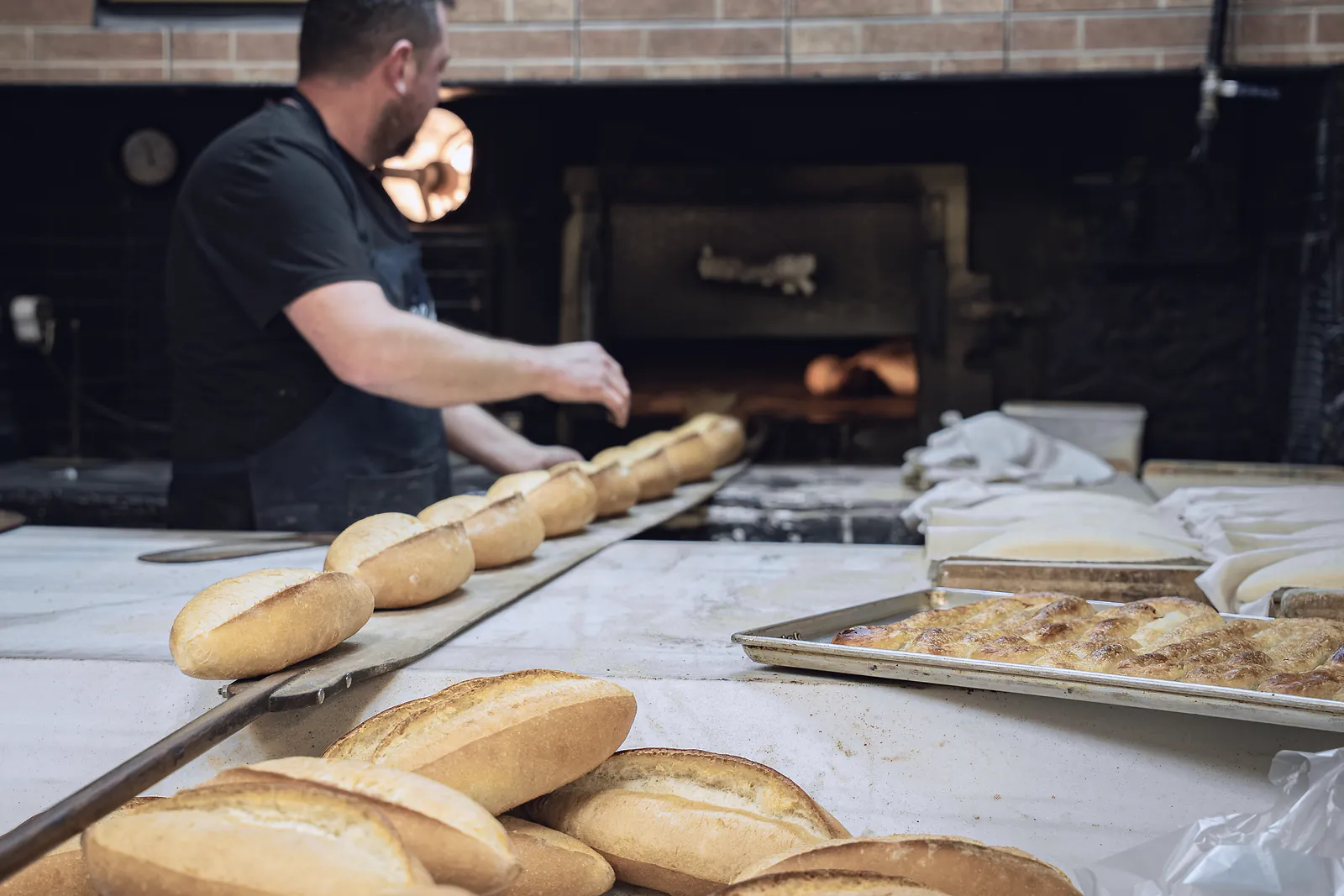 A baker loads fresh loaves on a long peel into a bakery's oven