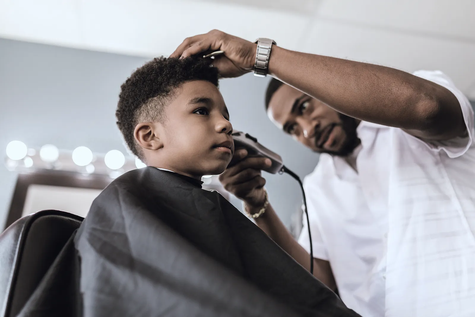 A barber trims a boy's hair with clippers in a bright barbershop
