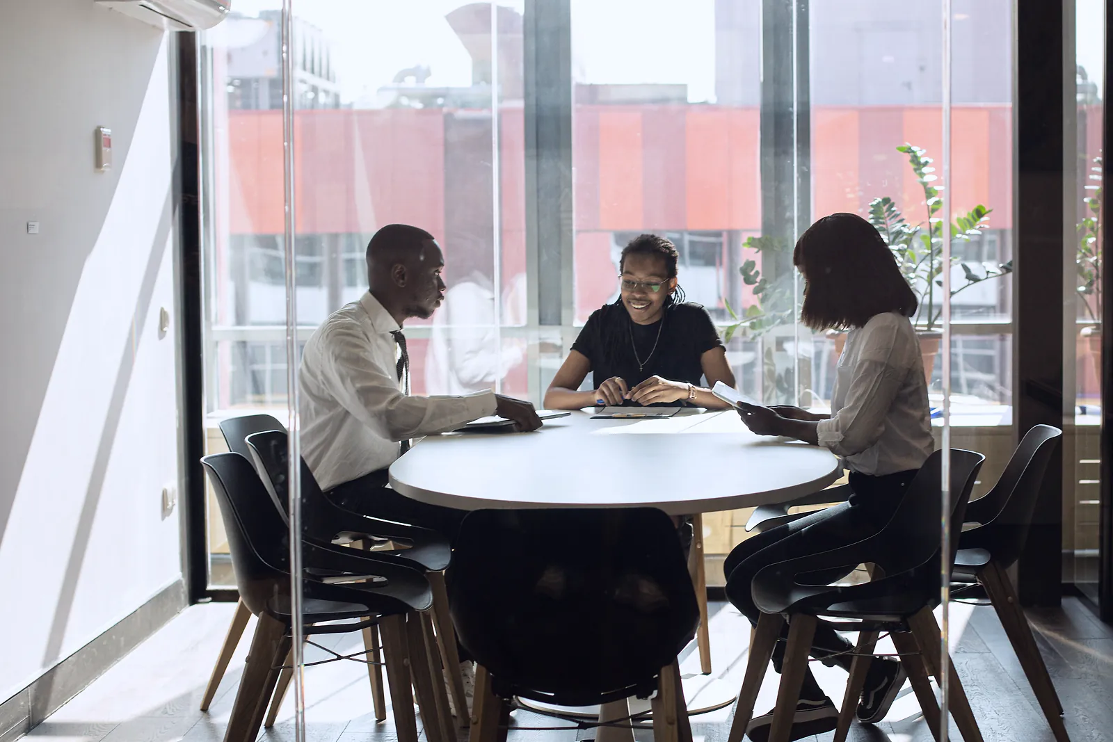 Three professionals meeting at a round table in a glass-walled meeting room