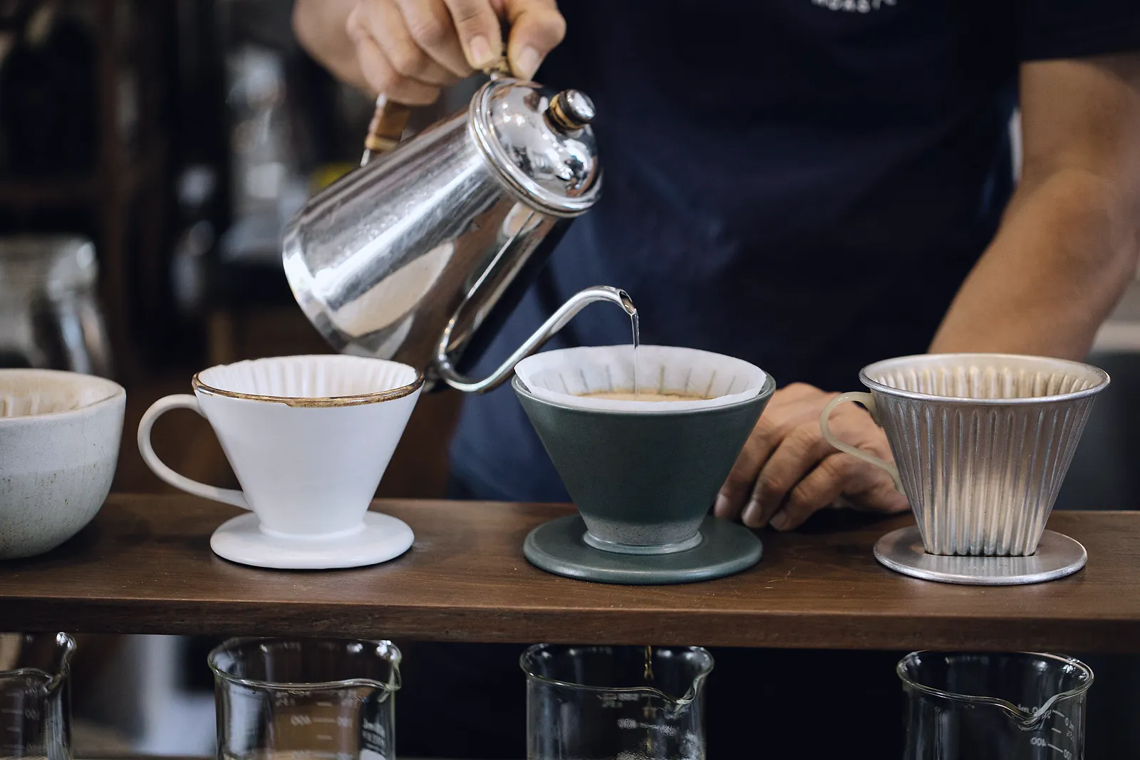 Barista pouring water into pour-over coffee drippers on a cafe's wooden coffee bar