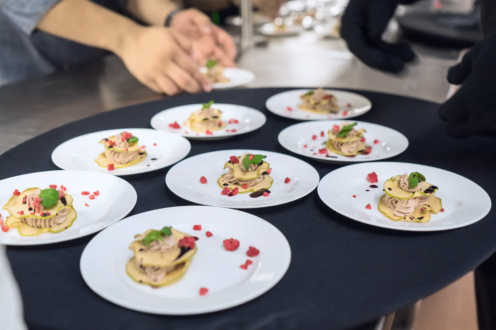 Matching plated starters are finished on a service tray in a catering kitchen