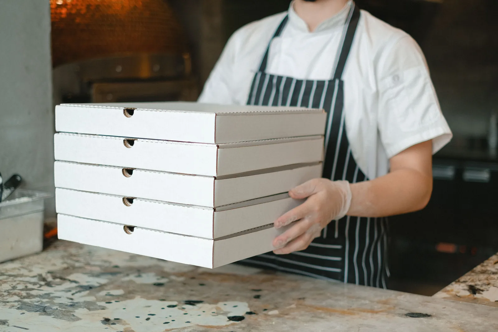 Chef in whites carrying a stack of delivery boxes through a commercial cloud kitchen