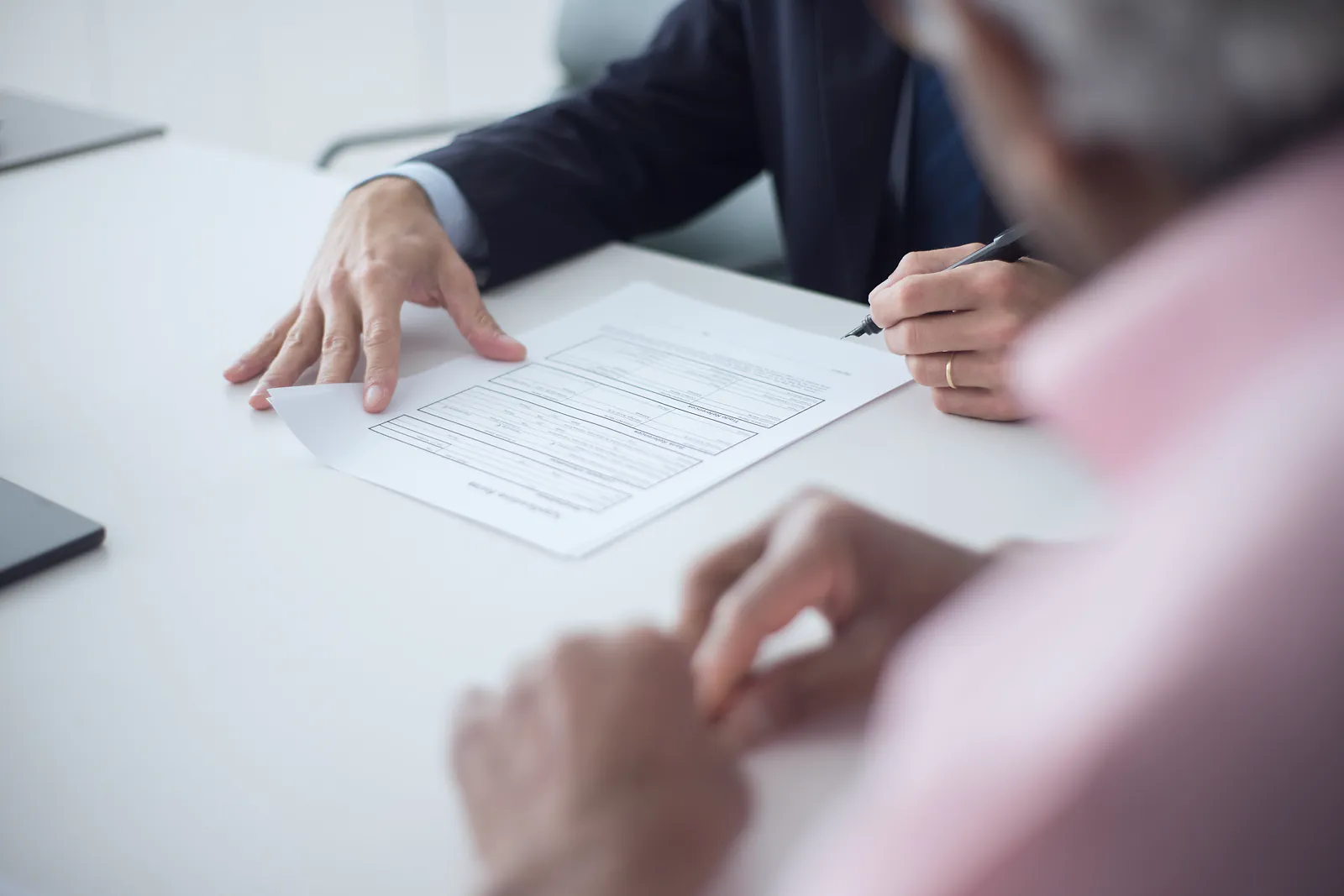 Two people go over an agreement across a white table before it is signed