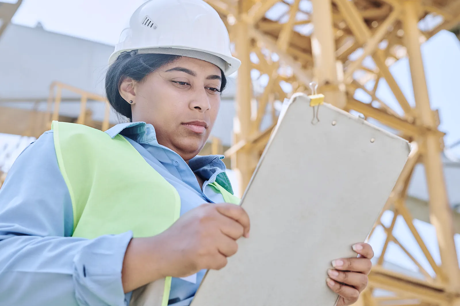 Site engineer in a hard hat and safety vest checking her clipboard at a construction project
