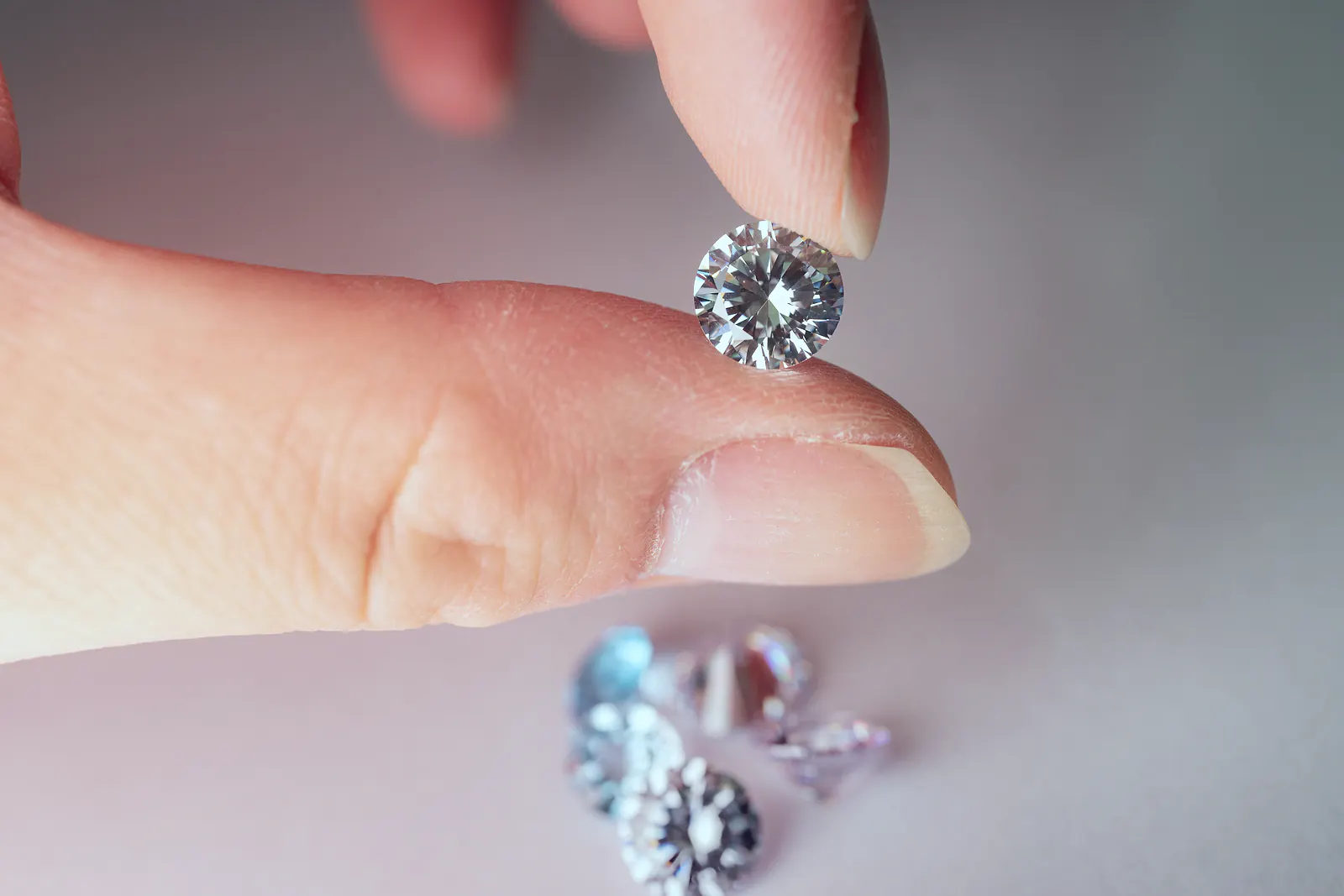 Fingers hold a round brilliant-cut diamond above a small group of loose stones