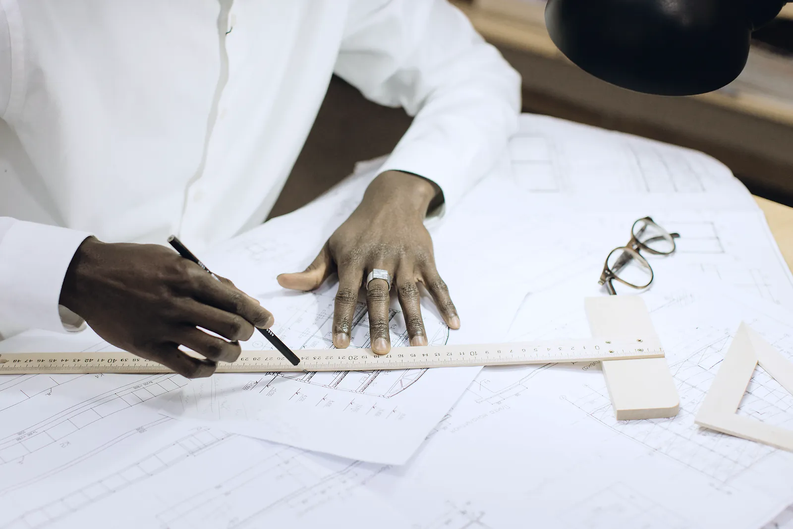 An engineer in a white shirt marks technical drawings against a long ruler