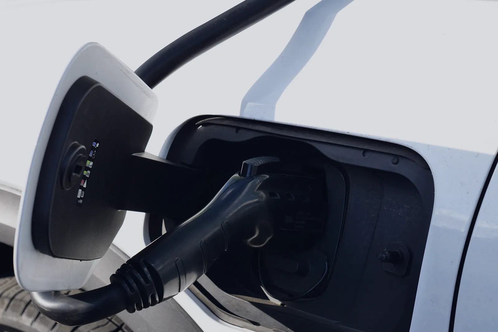 Charging connector plugged into the port of a white electric car