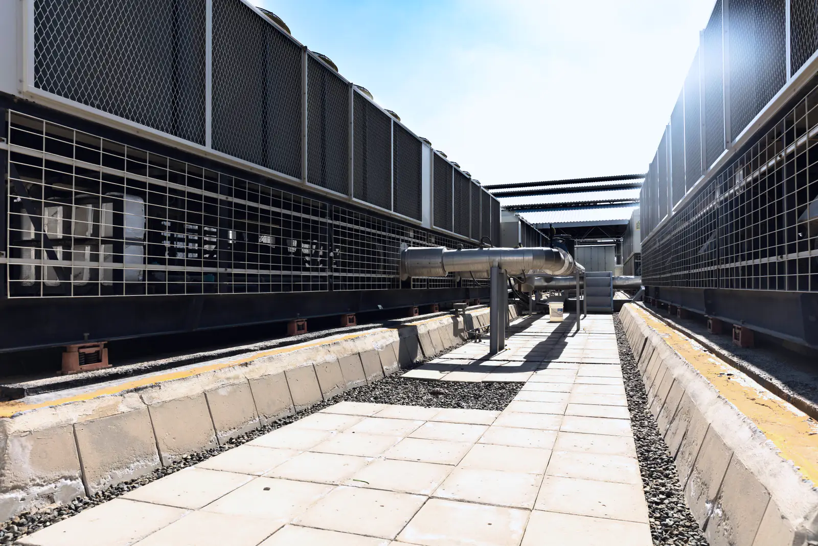 Rows of air-cooled chillers line a clean walkway on a commercial building's roof