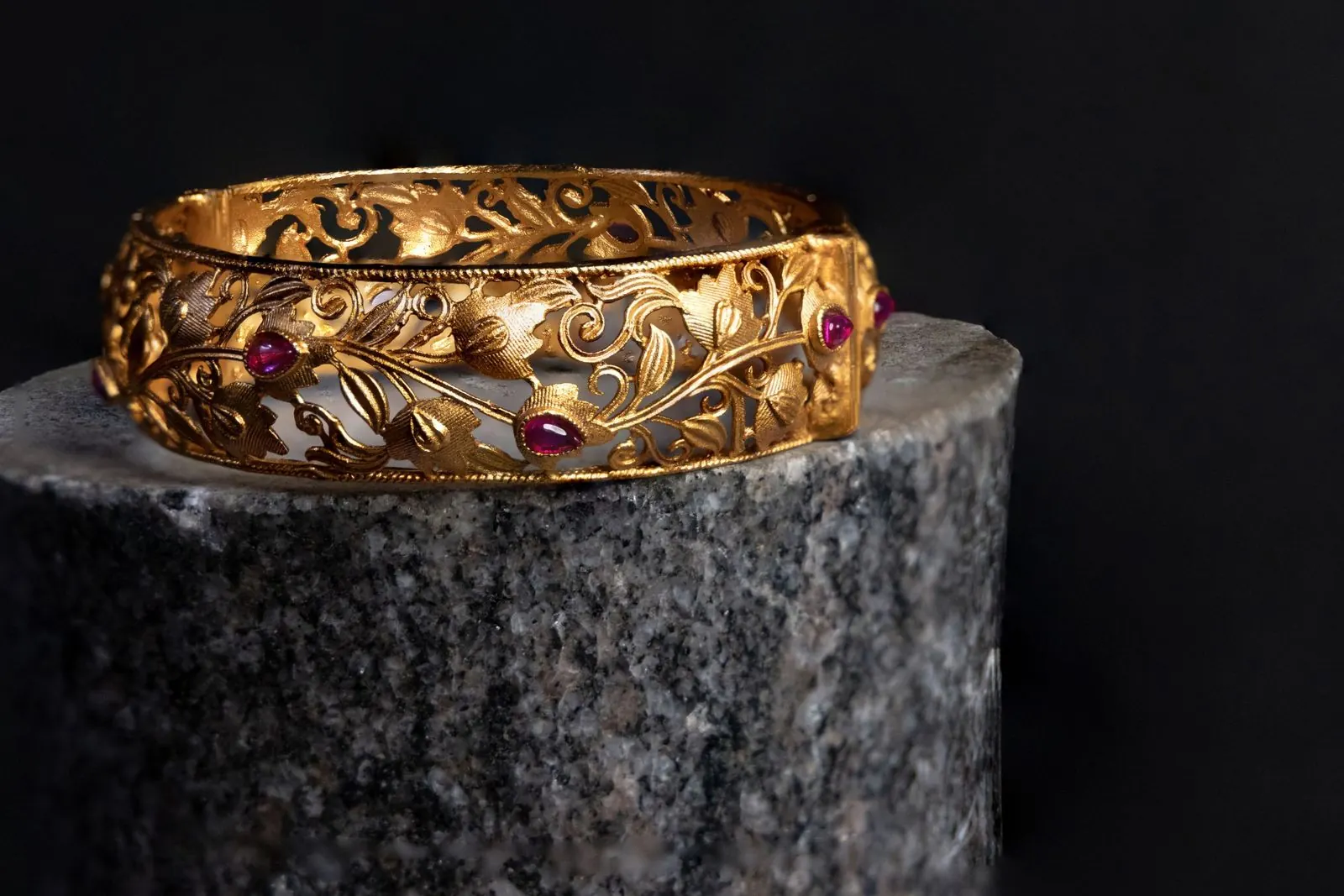 Gold bangle set with rubies displayed on a dark stone plinth