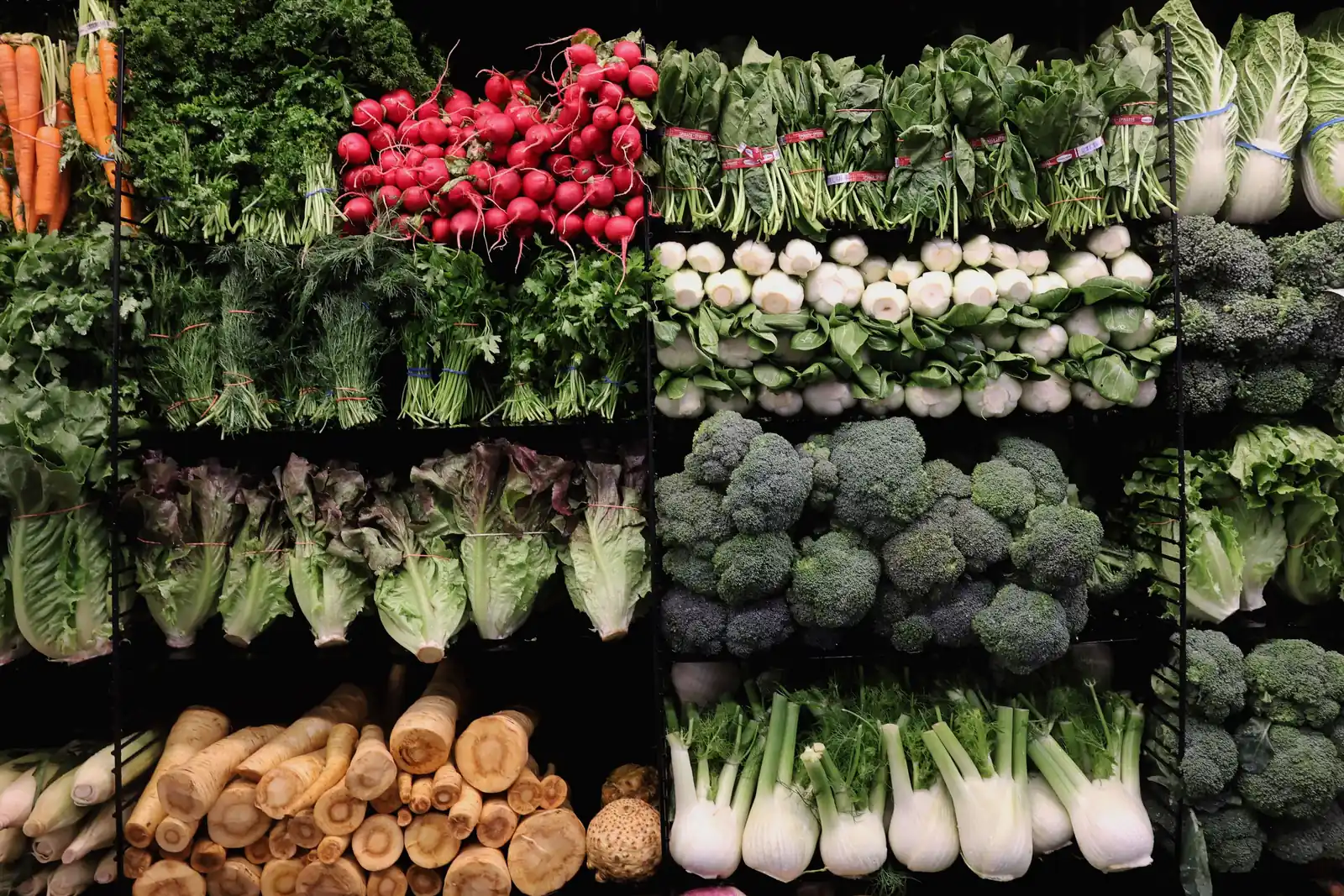 Fresh vegetables stacked on dark shelving in the produce section of a grocery store