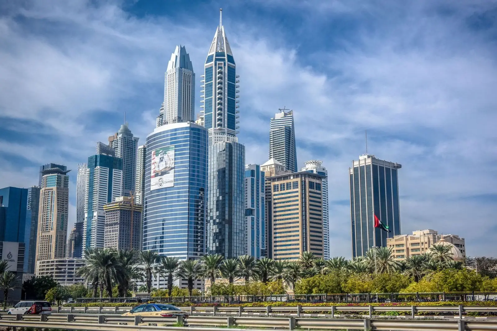 Dubai business district skyline of glass towers and palms, with the UAE flag flying