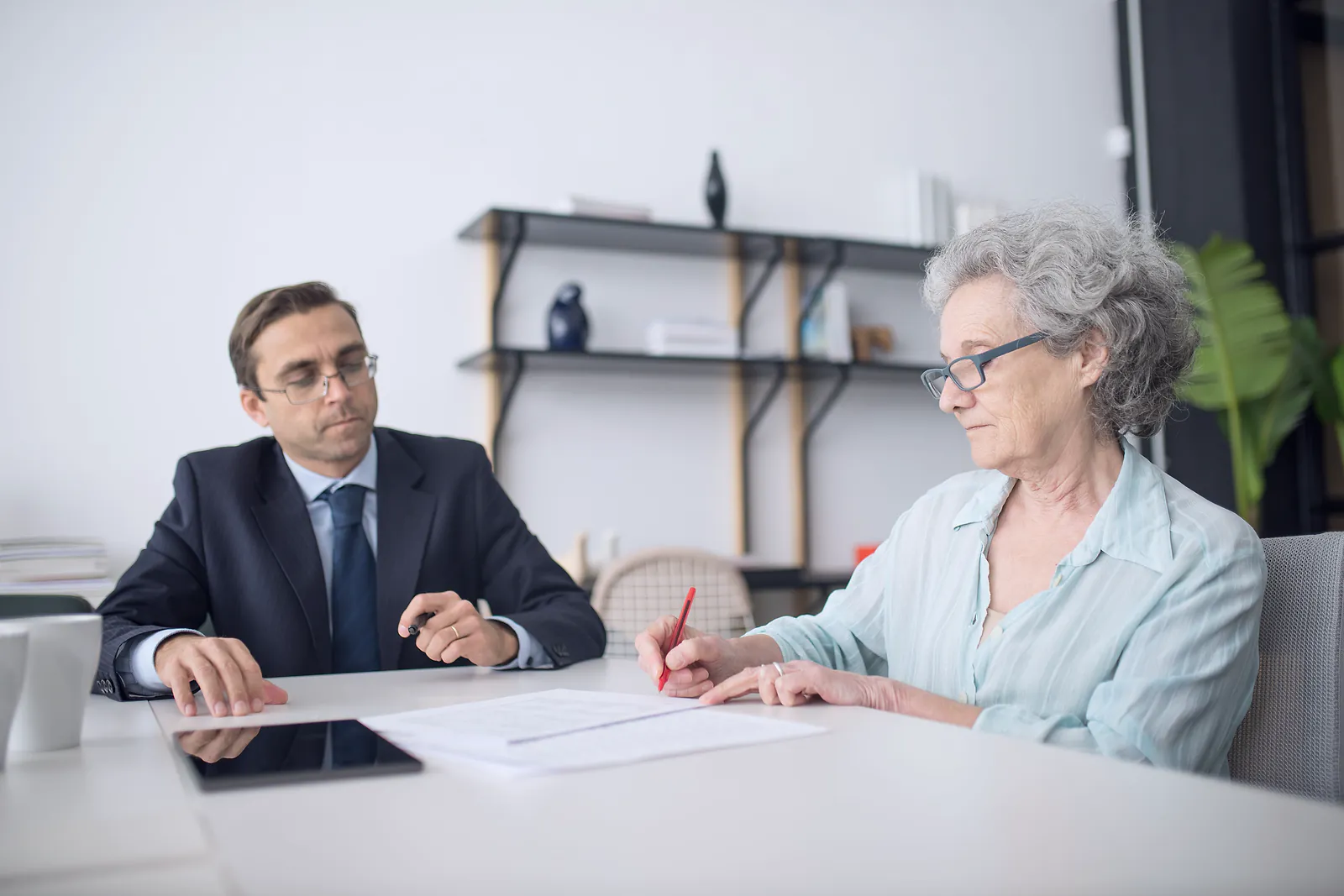 A legal adviser in a suit watches a client mark up a document at a desk