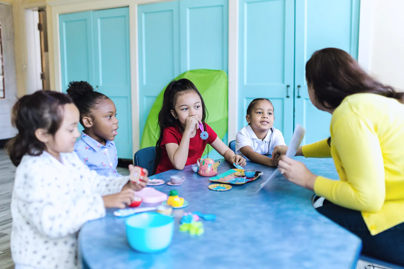 A nursery teacher leads four young children in a play session at a table