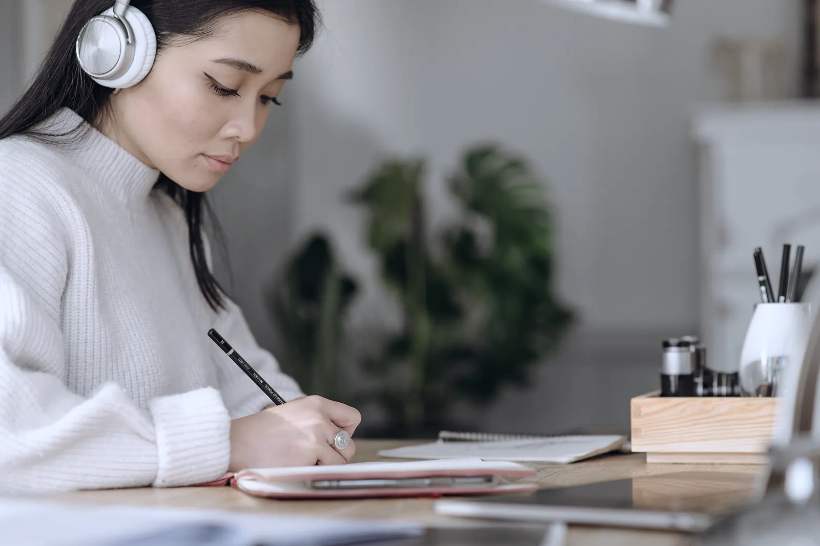 A learner in headphones takes notes beside a laptop during an online lesson