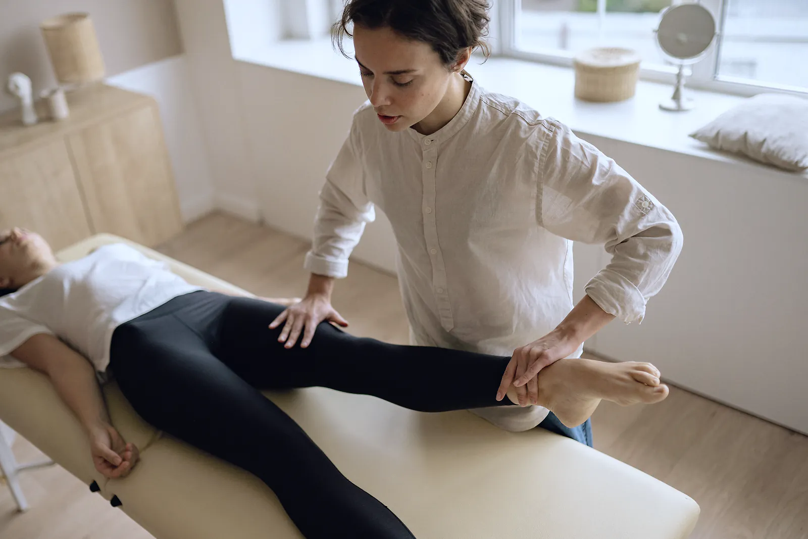 A physiotherapist moves a patient's leg through a hip exercise on a treatment table