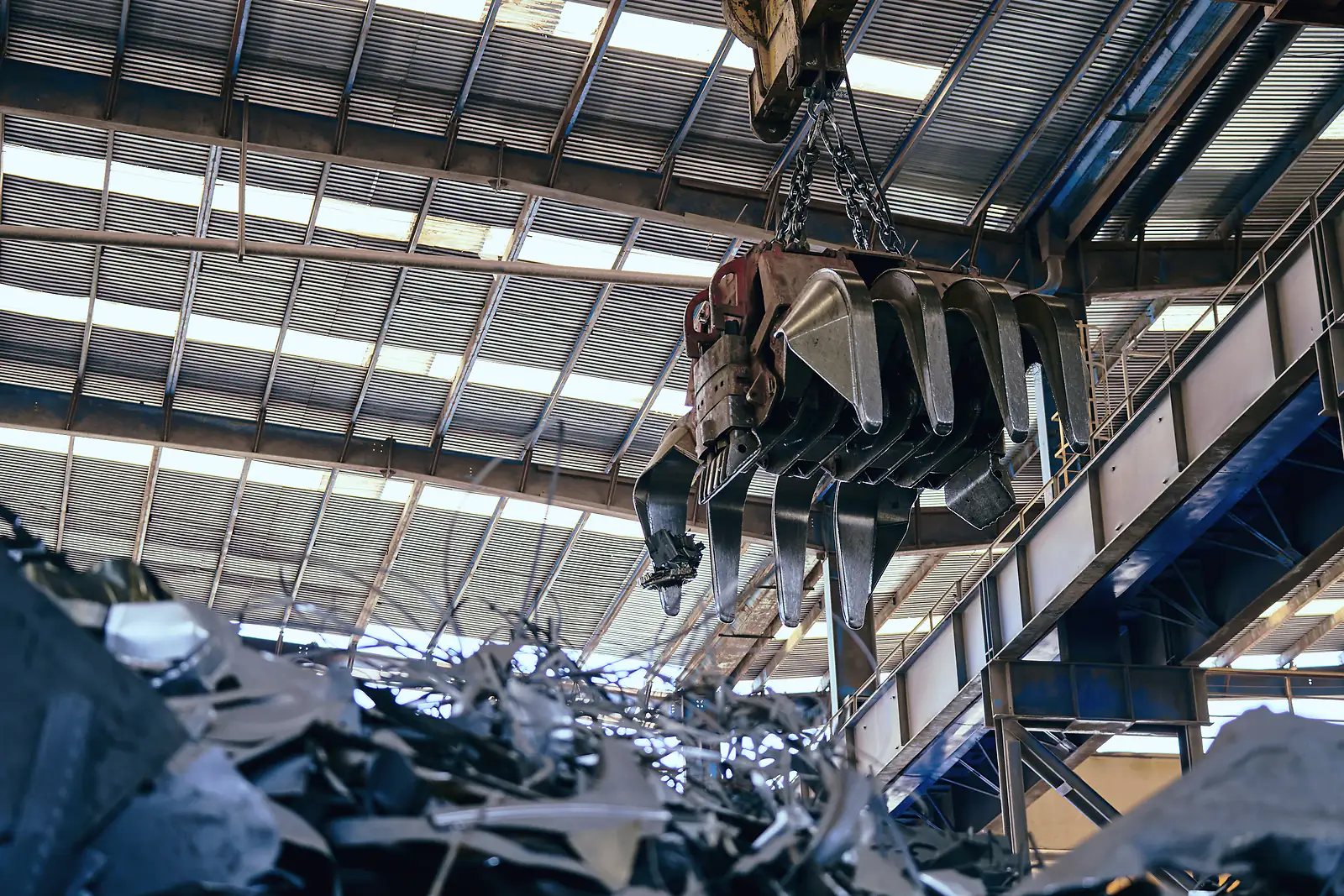 A crane grab lifts shredded steel scrap inside a covered scrap metal yard