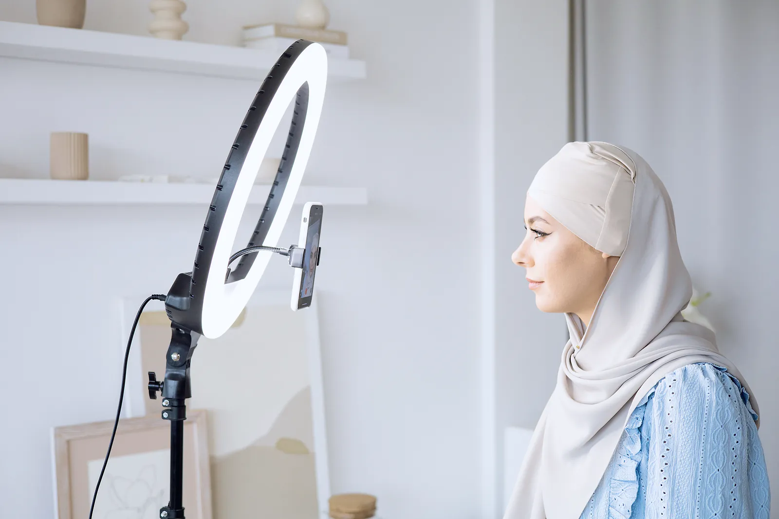 Content creator in a hijab facing a phone on a ring light before recording