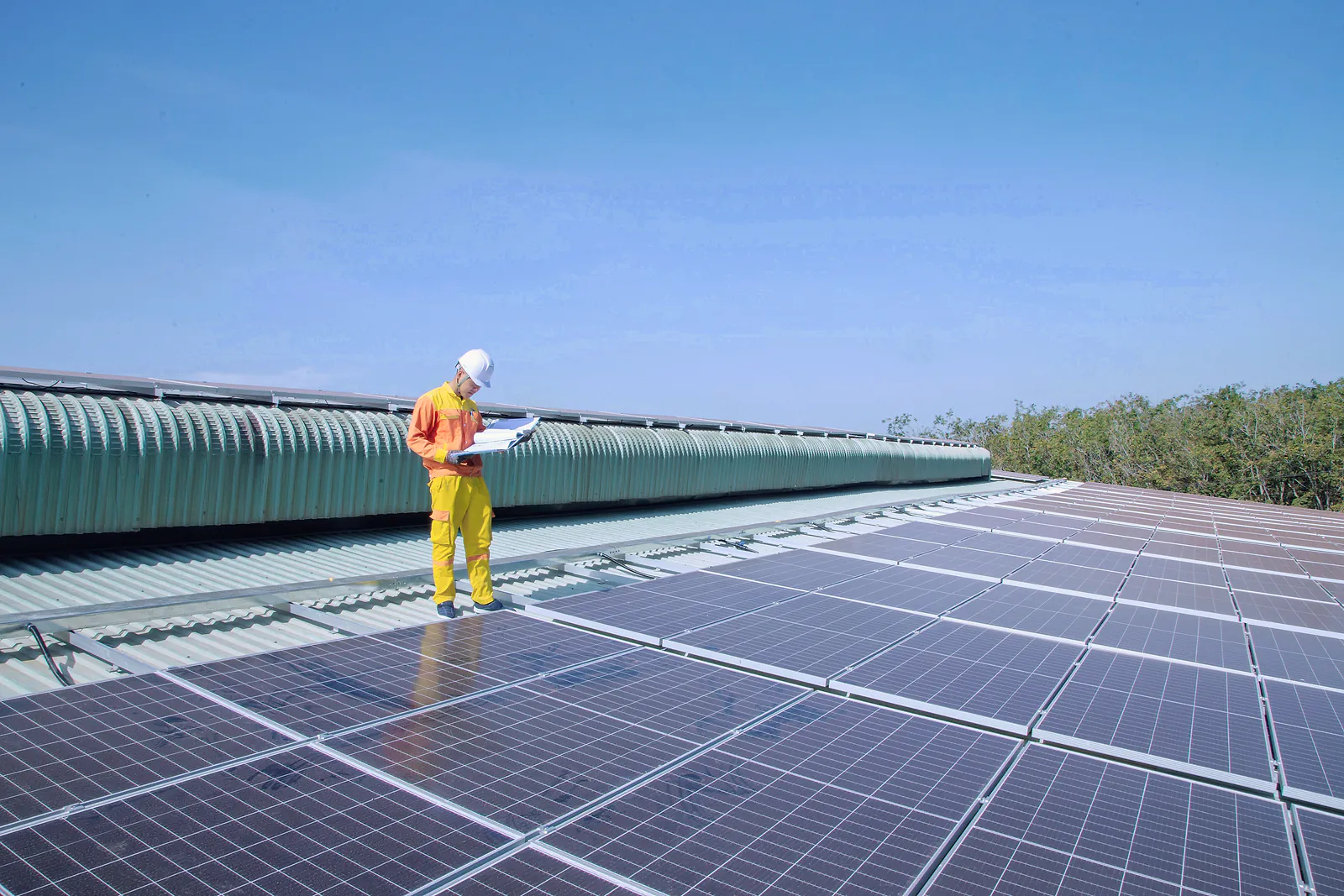 Solar technician in a hard hat checking plans on a commercial rooftop solar array