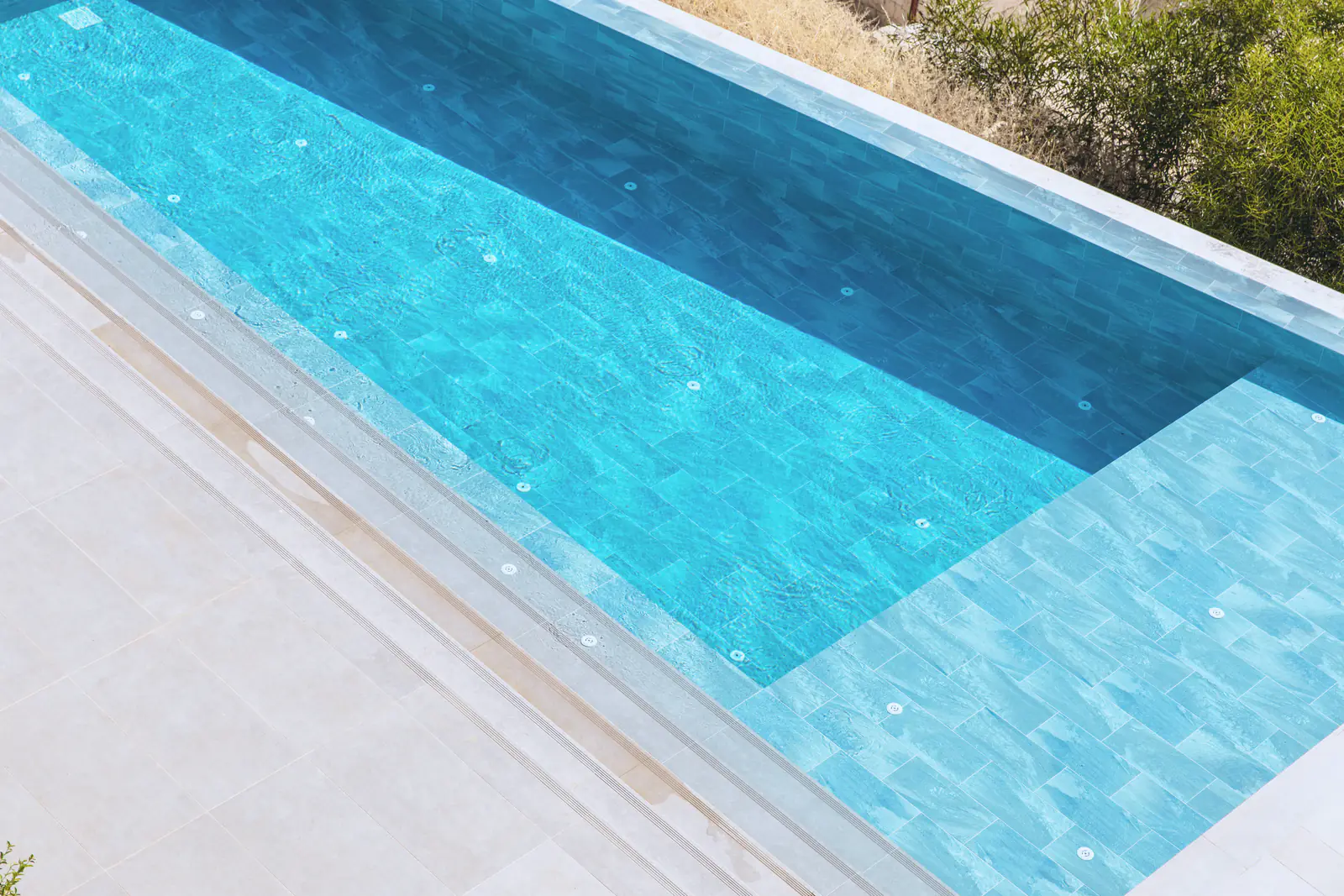 Clear blue water in a clean tiled villa pool beside a pale stone deck