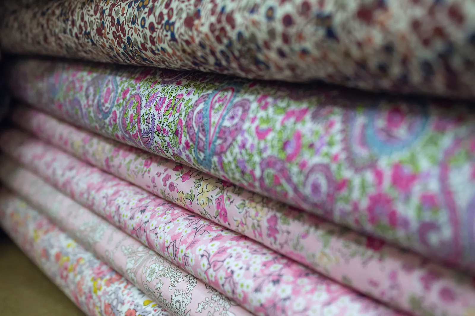 Folded bolts of printed cotton fabric stacked on a shelf in a textile store