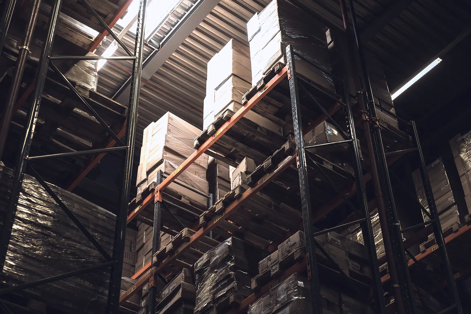 Shrink-wrapped pallets of boxed goods on high racking in a warehouse