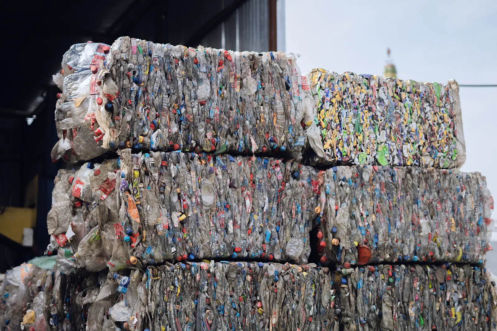 Compressed bales of plastic bottles stacked for recycling outside a sorting shed