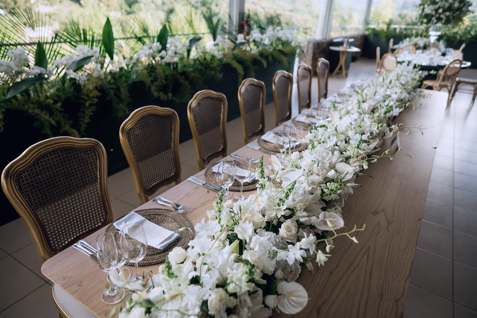 A long wedding table dressed with white orchids and roses, set for guests