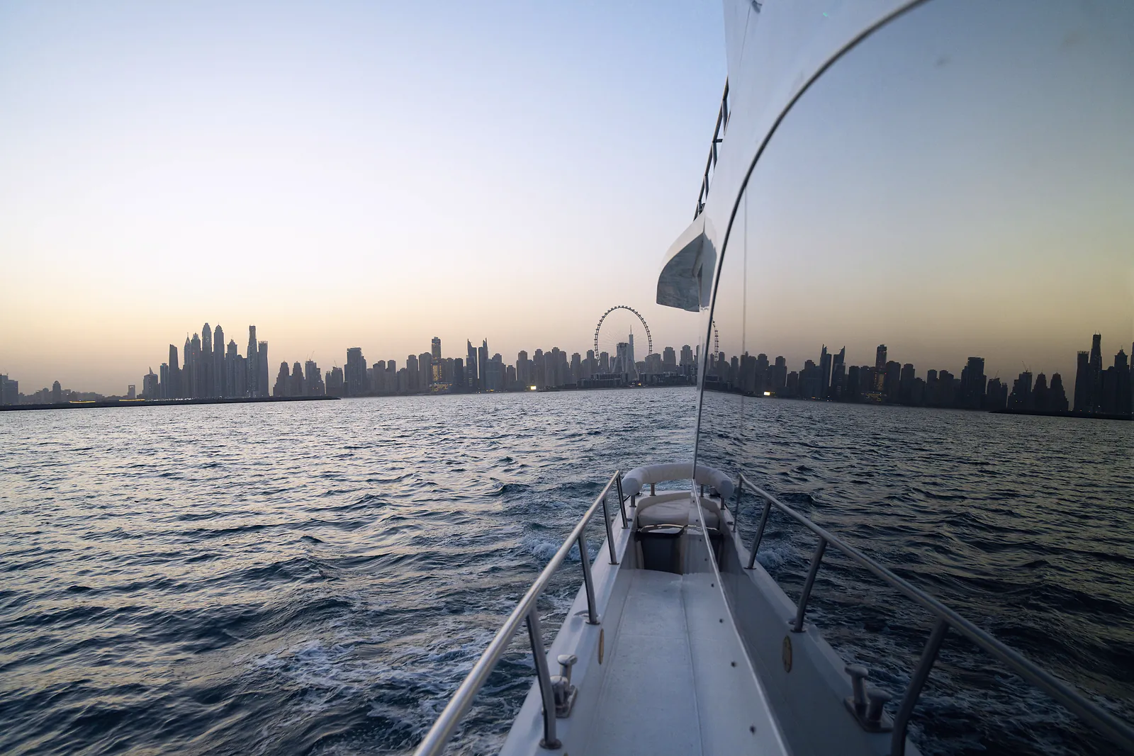 The Dubai Marina skyline at dusk, seen along the bow of a cruising yacht
