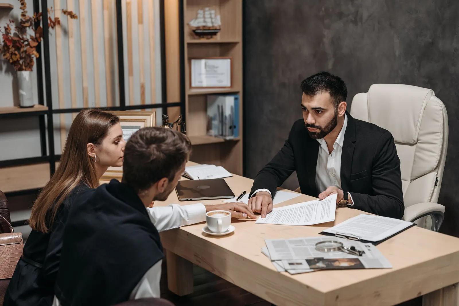 Advisor at his desk going through printed documents with two clients across the table