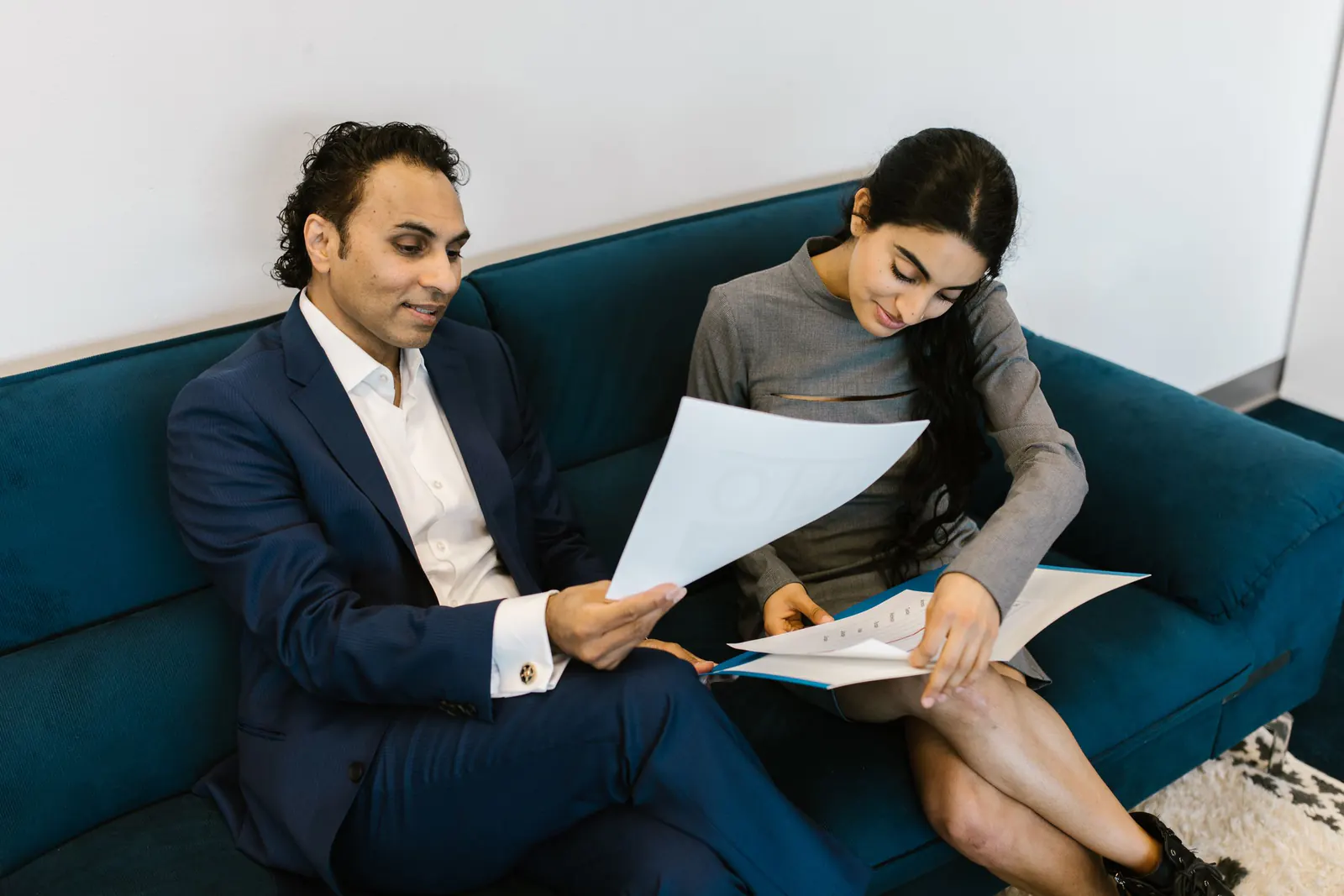 Advisor in a navy suit showing a client a document as they sit together on a sofa