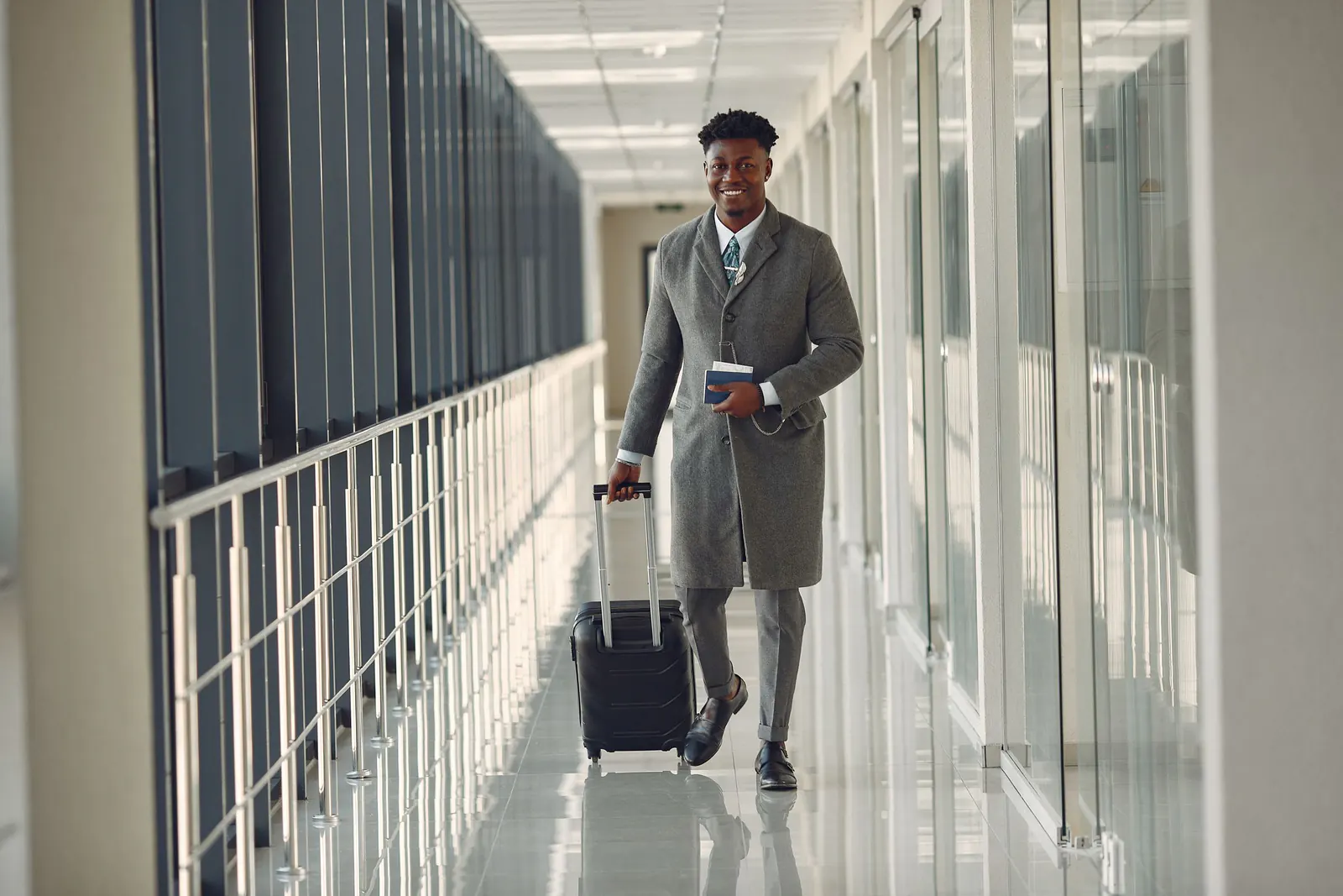 Traveller in a grey overcoat walking an airport corridor with his suitcase and passport