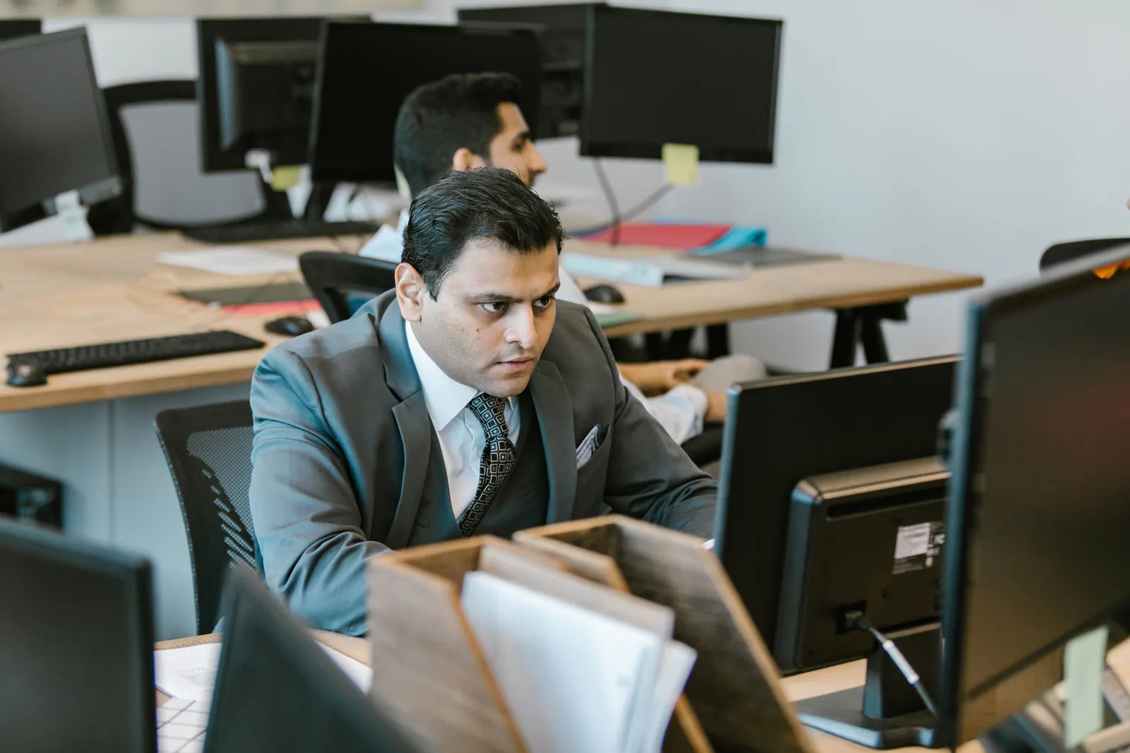 Professional in a grey suit at his workstation in a busy open-plan office