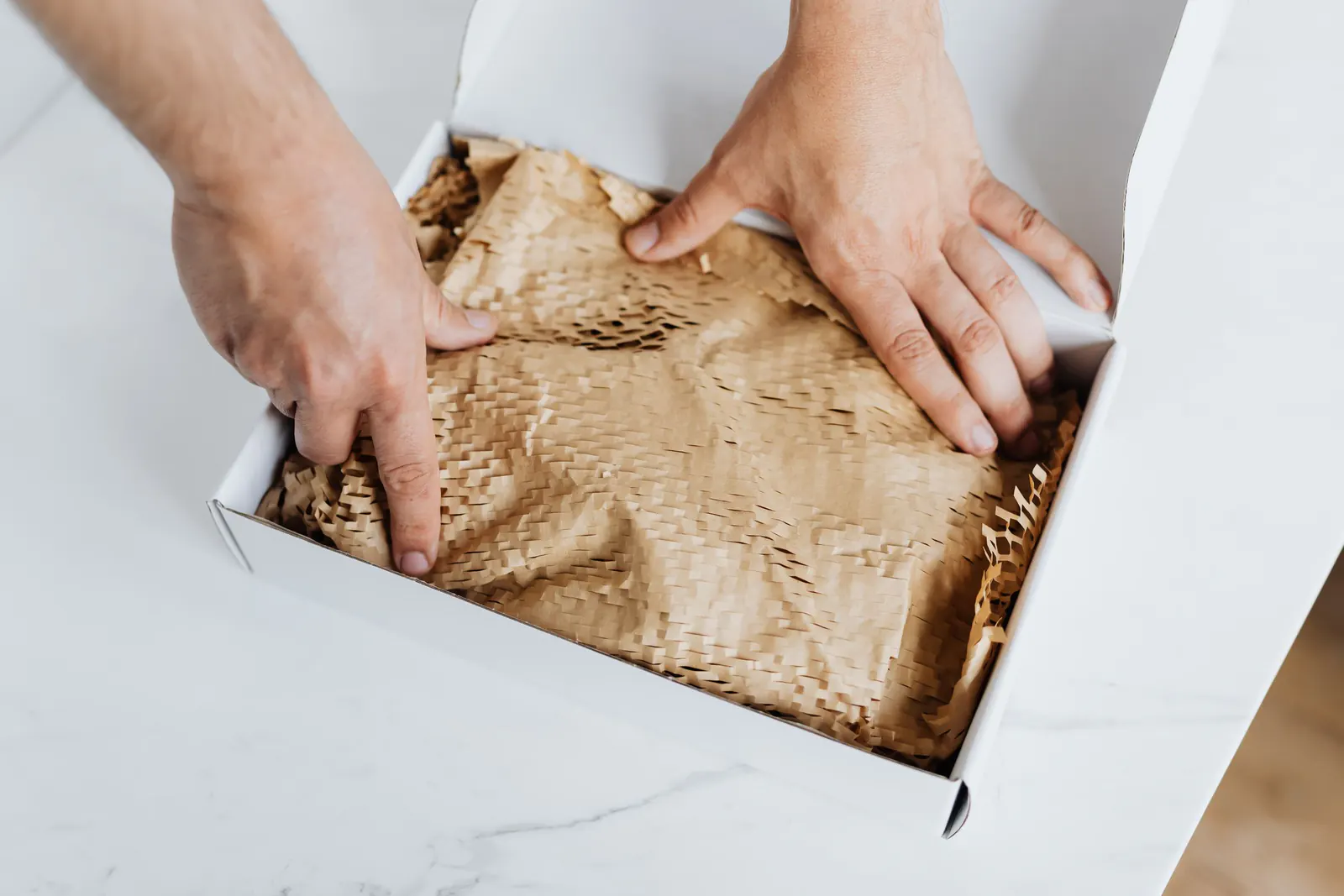 Hands packing an order into a white box lined with brown honeycomb paper