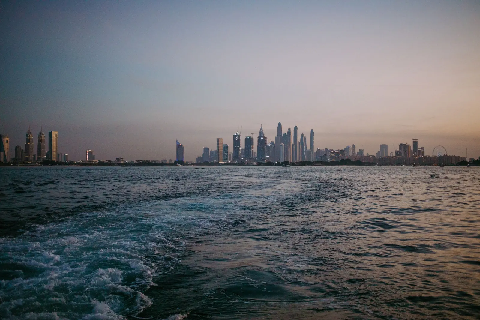 Dubai Marina skyline at dusk seen from a boat on the Gulf, with the wake in the foreground