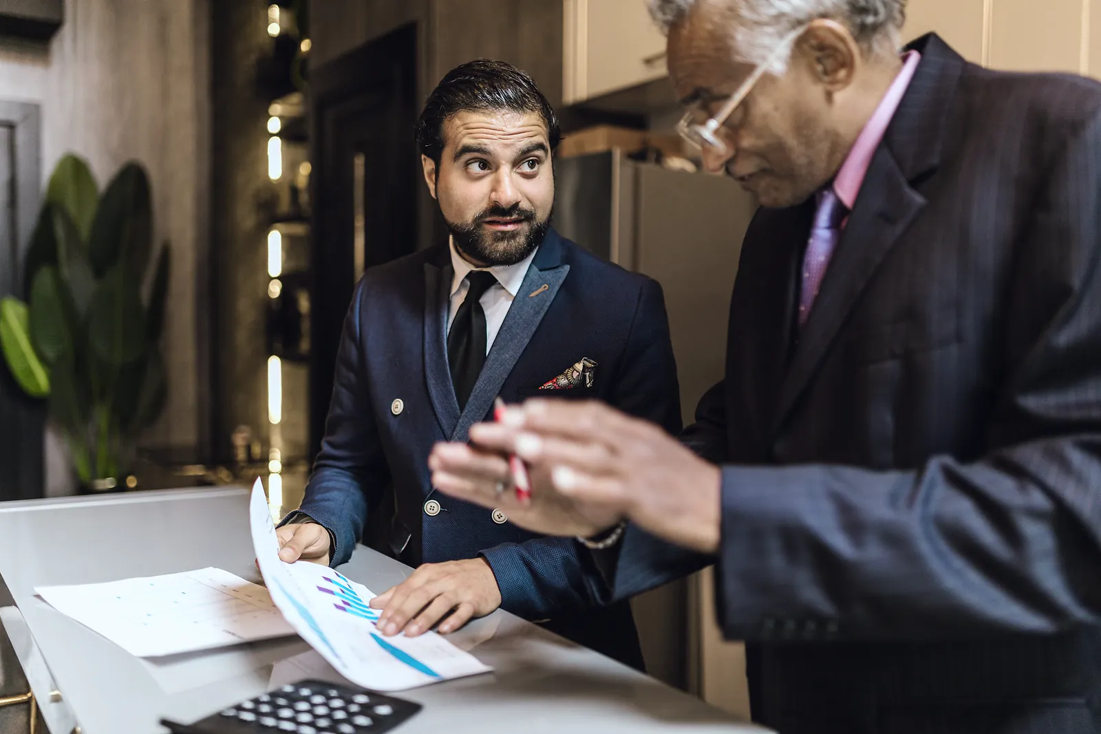 Senior advisor pointing a pen at a client's printed figures beside a calculator at an office counter