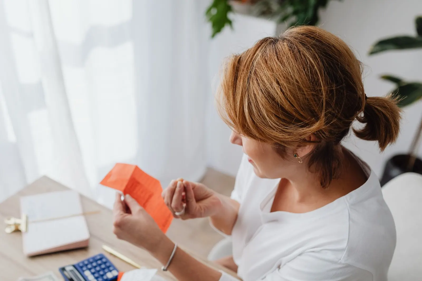 Business owner at her desk holding up a receipt to check it, with a calculator and papers in front of her