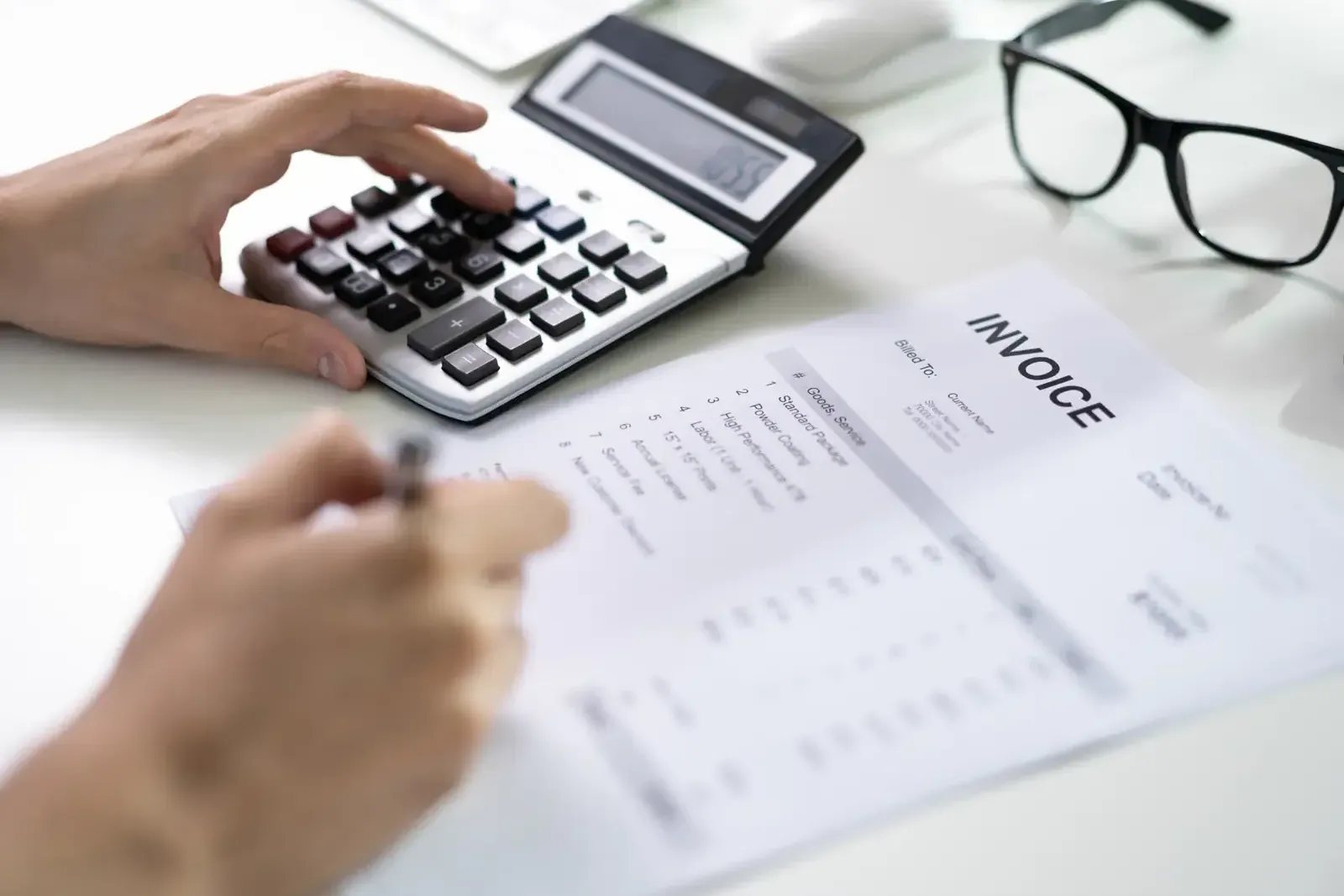 Hand on a calculator beside a printed supplier invoice being checked line by line