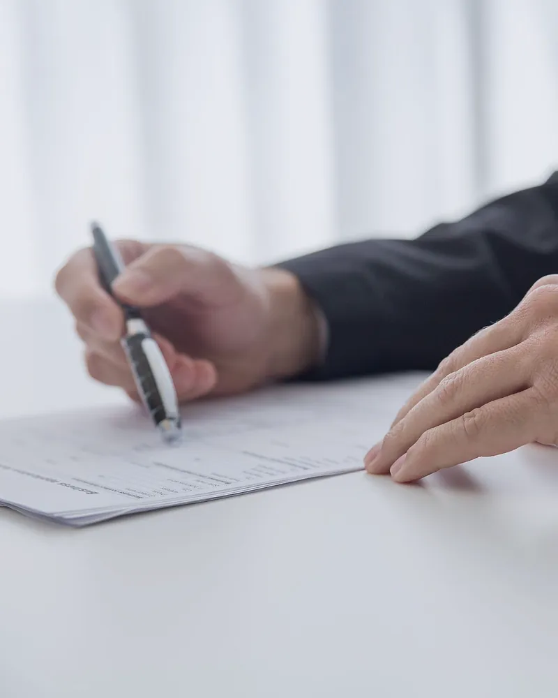 A hand with a pen going through a printed agreement on a white desk