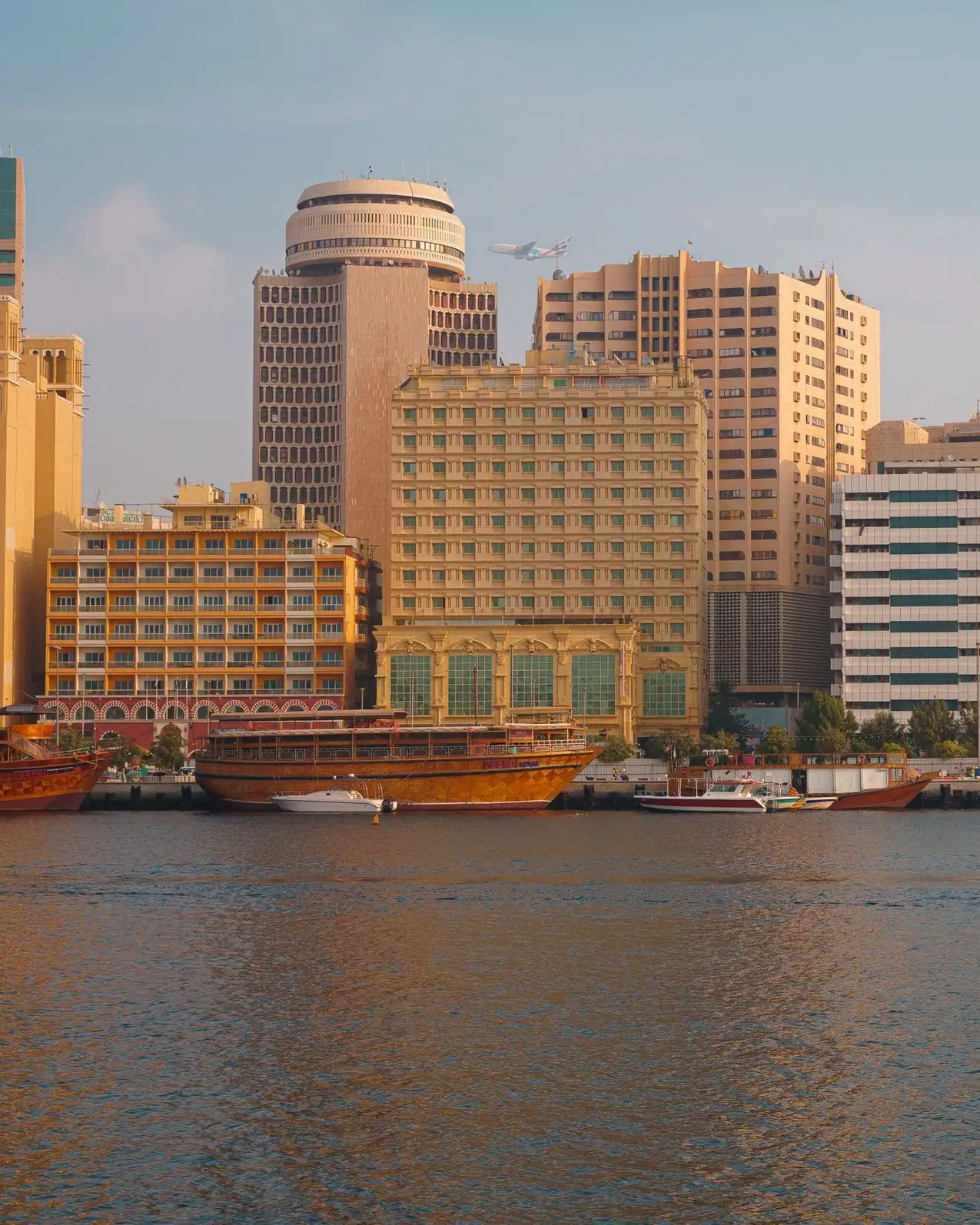 Deira's waterfront blocks in warm morning light, wooden dhows moored along Dubai Creek below
