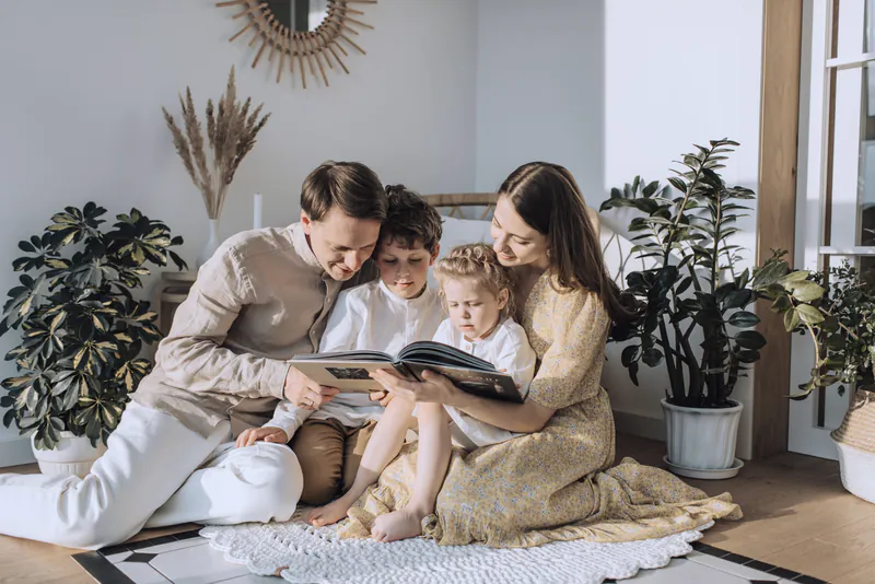 Parents reading a picture book with their two young children on the floor of a bright living room