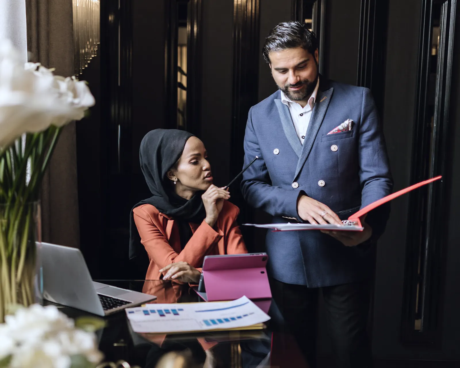Two business partners going through a red folder together beside a laptop in an office