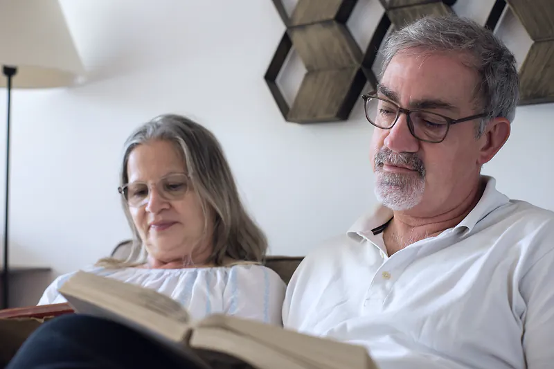 A retired couple reading a book together on the sofa at home