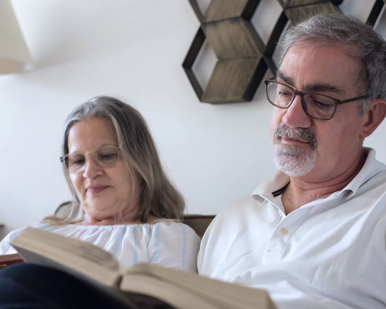 A retired couple reading a book together on the sofa at home