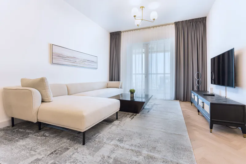 A bright living room with a cream corner sofa, sheer curtains and a balcony door