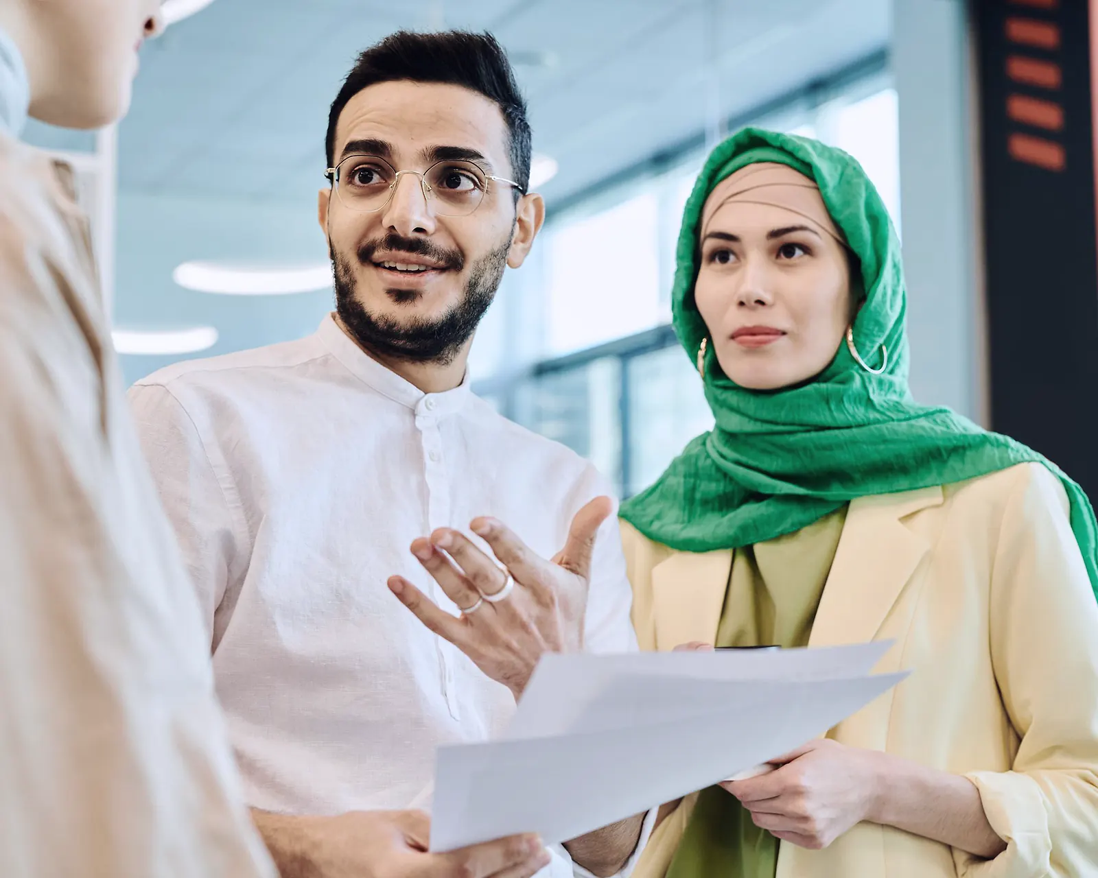 Two colleagues in an office talking over a printed document, one of them wearing a green headscarf